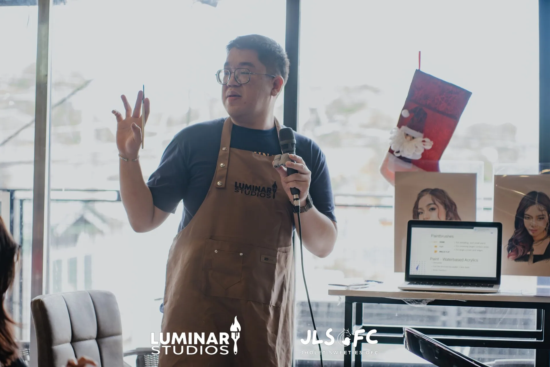 Charles Luminary in a Luminary Studios apron, holding a brush and microphone while teaching a figure painting workshop